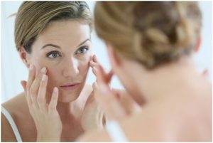 سيدة تنظر إلى تجاعيد وجهها أمام المرآة