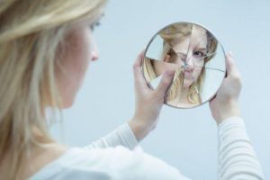 فتاة تحمل مرآة مكسورة كإشارة عن الإيذاء النفسي