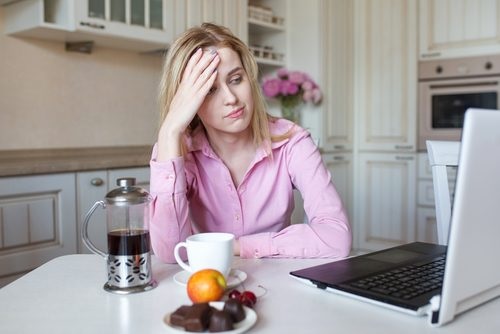 سيدة تضع يدها على رأسها وتجلس في المطبخ لتشرب القهوة